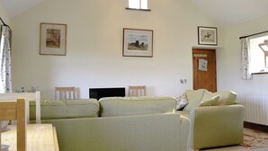 A cozy living room with a high ceiling, wooden beams, and a fireplace. There are three sofas and a television in the center.
