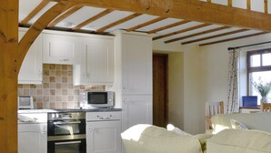 A kitchen with white cabinets, a microwave, and an oven. There is a wooden ceiling beam structure.