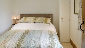 A neatly made bed with floral bedding, a bedside lamp, and a door with a mirror and curtain.