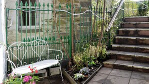 A stone building with a green metal fence, a white bench, and a staircase leading to a higher level.