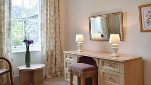 A bedroom with a vanity, two lamps, a mirror, a chair, and a vase with flowers.