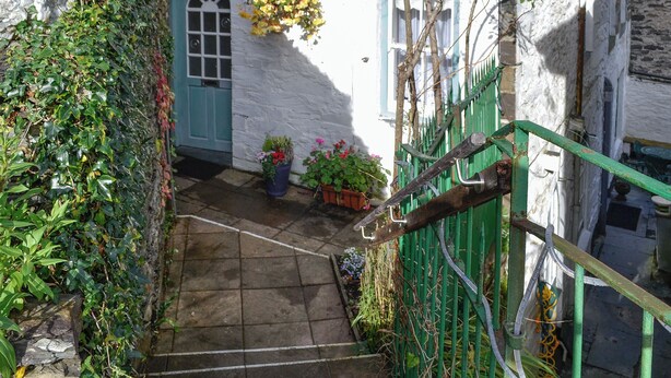A narrow stone staircase leading to a door with a blue frame, surrounded by greenery and potted plants.