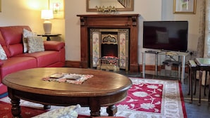 A living room with a red sofa, a wooden coffee table, a fireplace with a mirror above it, and a television on a stand.
