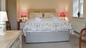 A neatly arranged bedroom with a bed, bedside lamps, a dresser, and a window with a view.