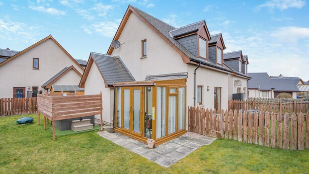 A residential house with a fenced backyard, a wooden deck, and a conservatory.
