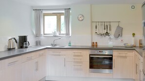 A modern kitchen with a built-in oven, a coffee maker, and a clock on the wall. - 3 bedroom accommodation in St Gennys, Bude (St Gennys, Bude)