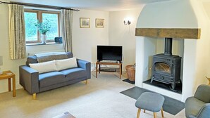 A living room with a sofa, TV, fireplace, and a window with curtains. - 3 bedroom accommodation in St Gennys, Bude (St Gennys, Bude)