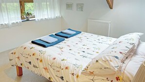 A bedroom with a bed, a window with curtains, a radiator, and a wooden ceiling beam. - 3 bedroom accommodation in St Gennys, Bude (St Gennys, Bude)