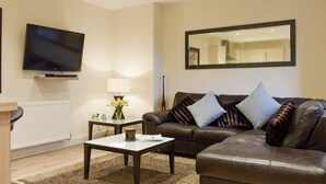 Een woonkamer met een flatscreentelevisie, een bank, een salontafel, een lamp en een spiegel aan de muur.