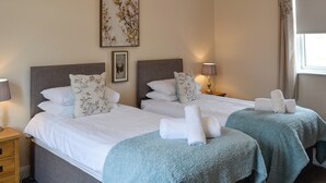 A hotel room with two beds, a bedside table with a lamp, a wall art piece, and a window with curtains. - Liftingstane Cottage (Closeburn, near Thornhill)