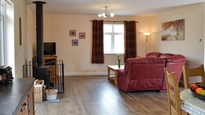 A living room with a fireplace, a sofa, a dining table with chairs, and a painting on the wall. - Liftingstane Cottage (Closeburn, near Thornhill)