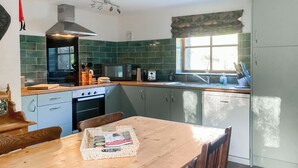 Une cuisine avec des carreaux verts, une table en bois et une fenêtre avec des rideaux.