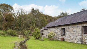 Une petite maison en pierre avec un toit en pente, une petite fenêtre et un chemin de pierre menant à un étang.