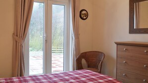 Une chambre à coucher comprenant un lit, une commode, un fauteuil en osier et une porte-fenêtre coulissante donnant sur un espace extérieur.