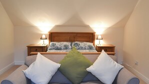 Une chambre à coucher avec un lit, deux tables de chevet avec des lampes, un canapé gris et un coussin vert.