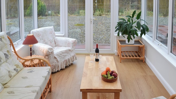 Une pièce chaleureuse, meublée de meubles en osier, avec une table en bois sur laquelle sont disposés des fruits et une bouteille de vin.