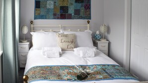 Een net opgemaakt bed met een kleurrijke quilt, een kussen met de tekst 'Live Laugh Love' en een decoratief glas op het bed.