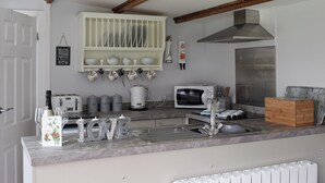 Een keuken met een ingebouwde magnetron, broodrooster en waterkoker. Boven de gootsteen staan planken met servies en bekers.