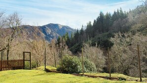 A grassy field with a wooden fence and trees, leading to a mountain range in the background.