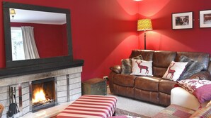 A living room with a fireplace, red walls, a leather sofa, and a striped ottoman.