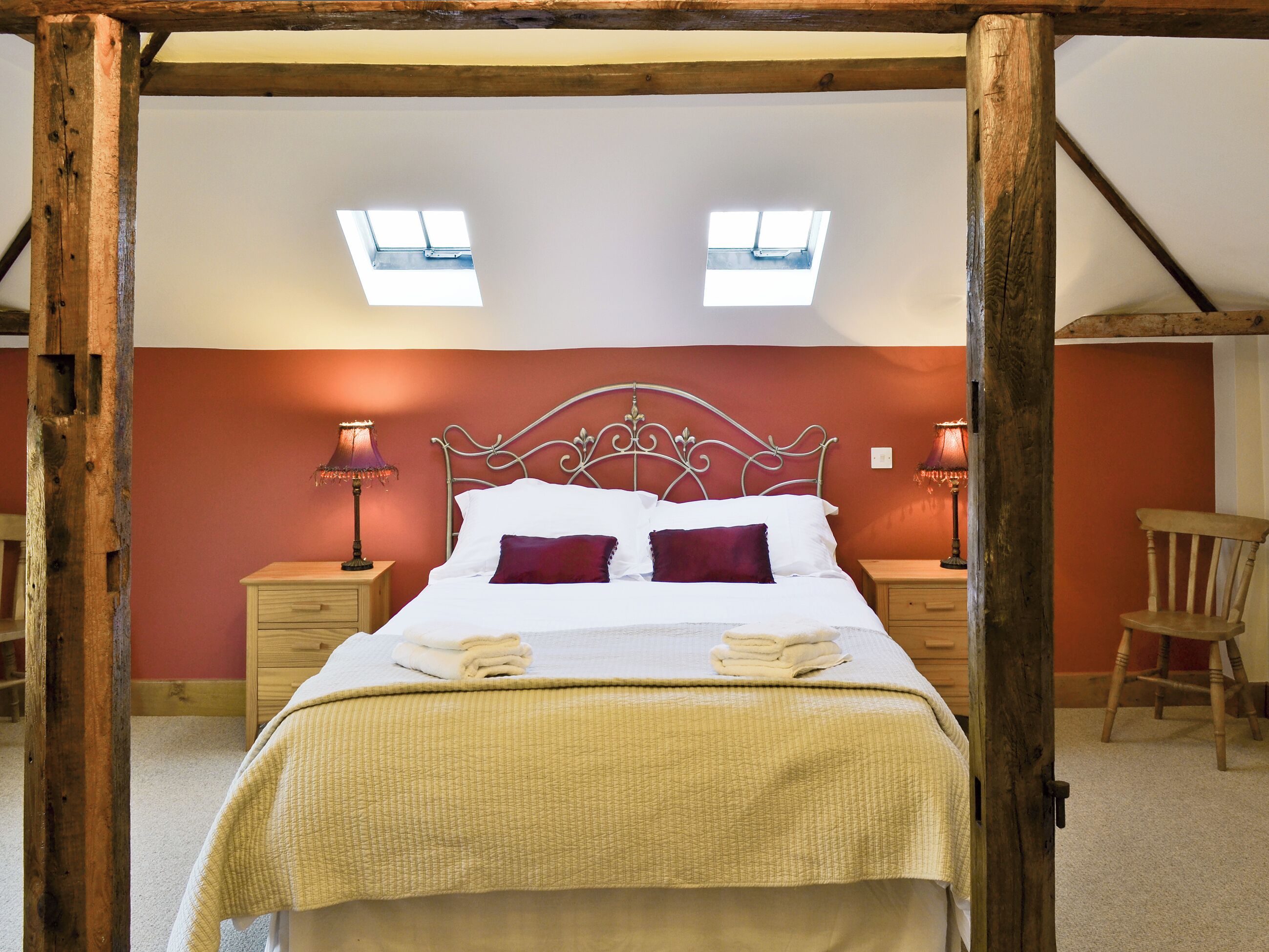 Une chambre à coucher avec un lit, deux lampes de chevet, une chaise en bois et une fenêtre.