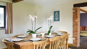 A dining area with a wooden table set for six, surrounded by wooden chairs. There are three potted orchids on the table, and a framed sign on the wall. - 4 bedroom accommodation in Uggeshall, near Southwold (Uggeshall, near Southwold)