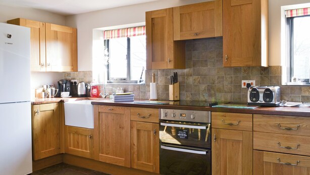 A kitchen with wooden cabinets, a Bosch refrigerator, a stove, and a window with a striped valance.