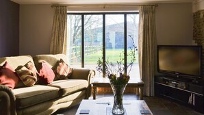 A living room with a sofa, a coffee table with a vase, a flat-screen TV, and a large window with curtains.