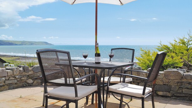 A table and chairs with an umbrella, overlooking a coastal view. - 1 bedroom accommodation in Llanaber, near Barmouth (Llanaber, near Barmouth)