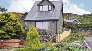 A house with a stone facade, a pitched roof, and a small garden with flowers and a conifer. - 1 bedroom accommodation in Llanaber, near Barmouth (Llanaber, near Barmouth)