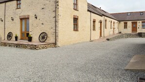 A building with a stone foundation, multiple windows, and a gravel driveway. - 3 bedroom accommodation in Llanynghenedl, near Holyhead (Llanynghenedl, near Holyhead)