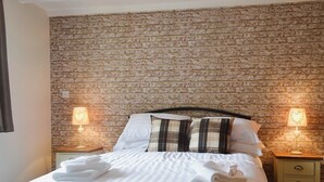 A neatly made bed with white linens and a striped duvet, two pillows with a plaid pattern, and two bedside lamps on wooden nightstands. - 3 bedroom accommodation in Llanynghenedl, near Holyhead (Llanynghenedl, near Holyhead)
