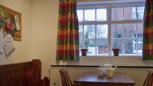 Ein Zimmer mit Holztisch, Stühlen, einem Fenster mit Vorhängen und einer Pinnwand mit Zetteln.