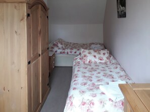 Quarto com uma cama de solteiro, um guarda-roupa de madeira e uma pequena mesa de cabeceira.