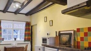 Eine Küche mit Holzbalkendecke, einem Fenster mit Vorhängen, einer Mikrowelle, einem Kühlschrank und einem Herd.