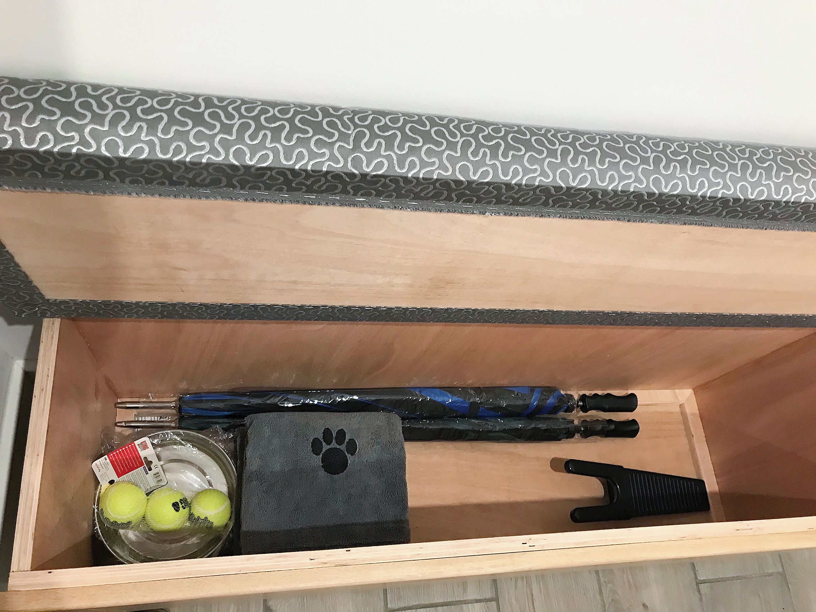 A wooden drawer with a patterned metal cover, a black object with a paw print, a tennis ball, and a blue and black object.