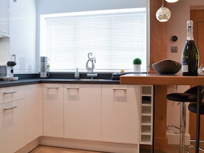 A modern kitchen with white cabinets, a black countertop, a sink, a wine bottle, and a hanging light fixture.