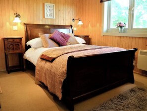 Ein Schlafzimmer mit Holzwänden, einem Bett, Nachttischen, Wandleuchten und einem Fenster mit Blick.