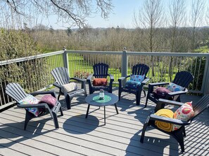 Eine Terrasse mit sechs Adirondack-Stühlen, einem runden Tisch und Blick auf eine grüne Landschaft.