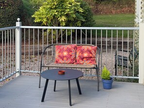 A patio with a metal fence, a wicker chair with a patterned cushion, a small round table, and a potted plant.