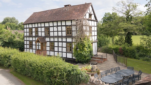 A traditional half-timbered house with a stone pathway leading to a patio area with outdoor seating. - 5 bedroom accommodation in Mathon, near Malvern (Mathon, near Malvern)