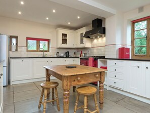 A kitchen with white cabinets, a wooden table, two stools, a red oven, and a window with a view of greenery.