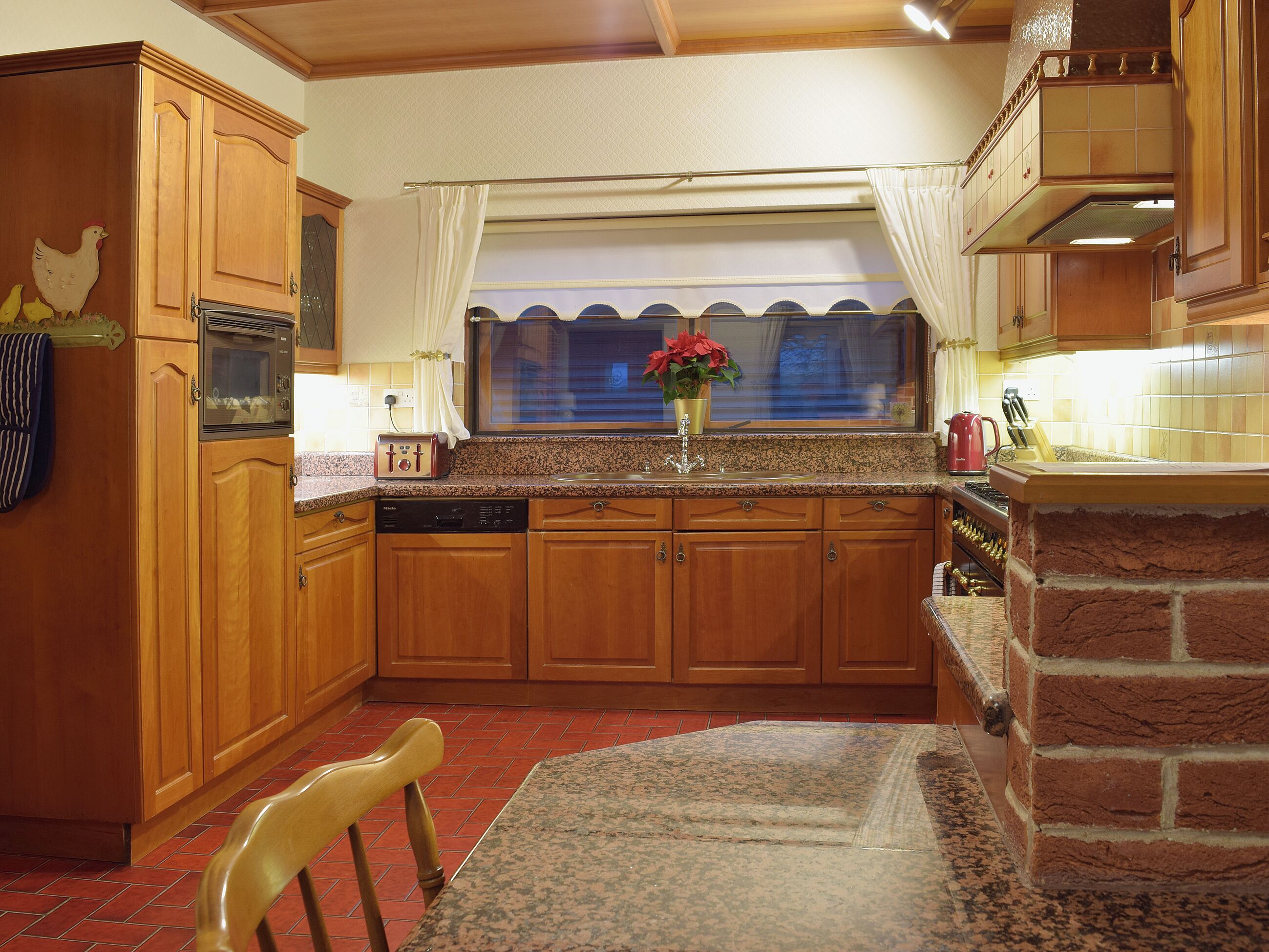 Cozinha com armários de madeira, bancada de granito, lava-louças, torradeira e parede decorada com tijolos.