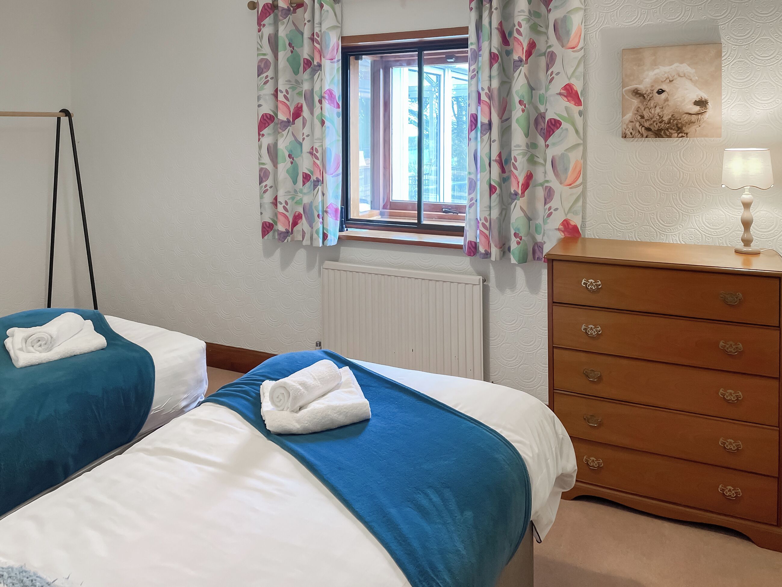 A bedroom with two beds, a dresser, a radiator, and a window with floral curtains.