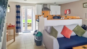 Ein Wohnzimmer mit einer Couch, einem Couchtisch, einem Mülleimer und einer Küchenzeile mit Schränken und einer Mikrowelle.