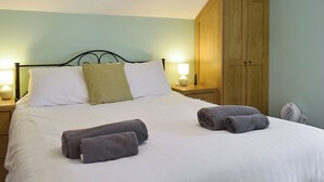 Ein ordentlich bezogenes Bett mit weißen und grünen Kissen, zwei zusammengerollte Handtücher und ein Holzschrank in einem Zimmer mit hellgrünen Wänden.