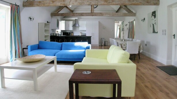 A spacious living area with a high ceiling, exposed wooden beams, a blue sofa, a yellow armchair, and a white coffee table. - 2 bedroom accommodation in Ludlow (Ludlow)