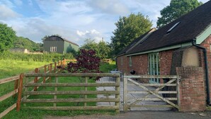 A rural property with a wooden gate, a brick building, and a green metal structure in the background. - 2 bedroom accommodation in Ludlow (Ludlow)