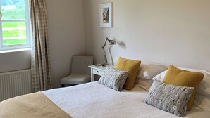 A neatly arranged bedroom with a bed, pillows, a chair, a bedside table, a lamp, and a window with curtains. - 2 bedroom accommodation in Ludlow (Ludlow)