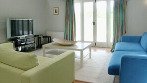 A living room with a television, a sofa, a coffee table, and a window with curtains. - 2 bedroom accommodation in Ludlow (Ludlow)